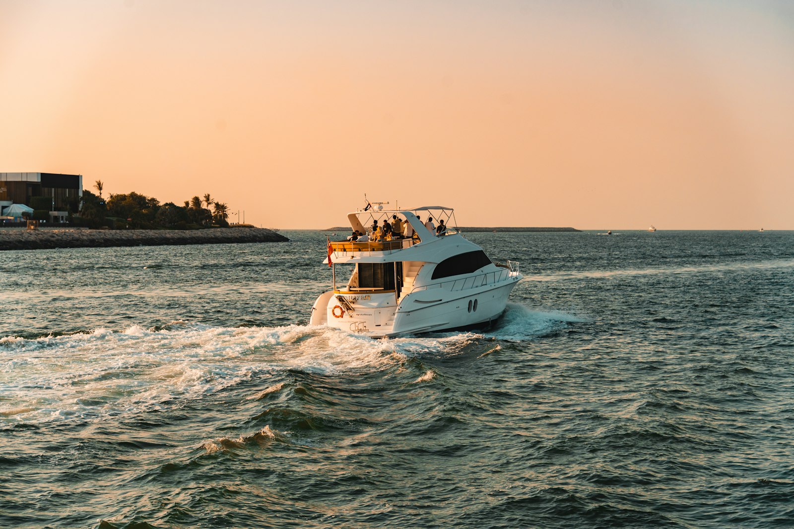 A white yacht cruises on the ocean at sunset.